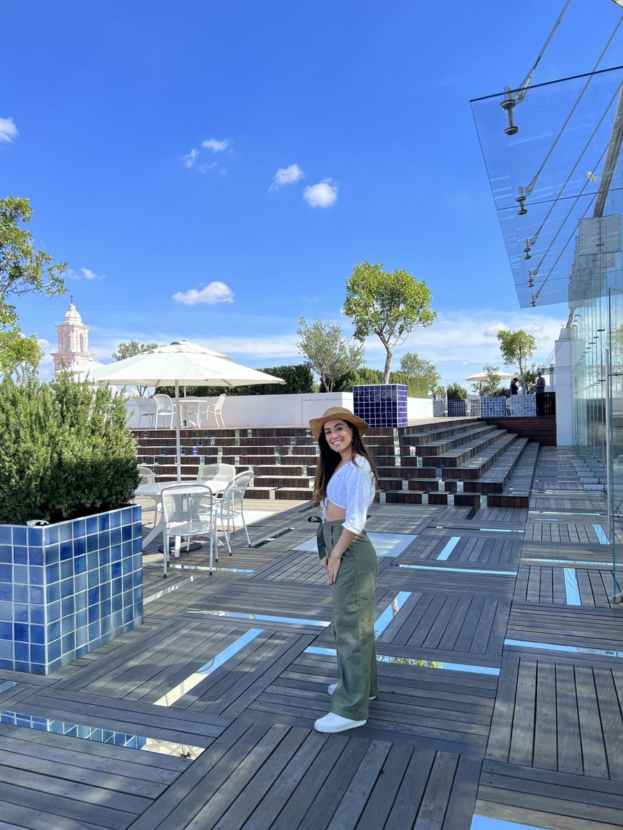 Valentina on a rooftop terrace with blue tiles, wooden steps and a church tower in the background